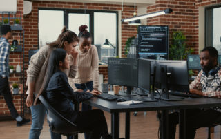 Mixed team of software engineers brainstorming ideas for new code library in front of computer screens